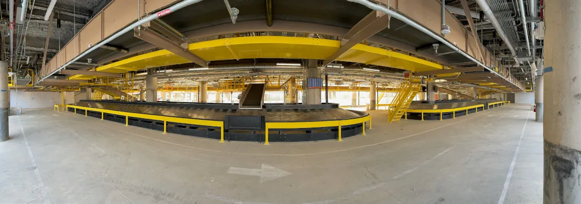 Airport baggage handling system with curved conveyor lines and yellow guard rails in a terminal